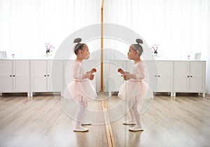 Little girl with down syndrome at ballet class in dance studio, standing in front of mirror. Concept of integration and