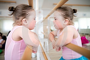 Little girl with down syndrome at ballet class in dance studio, standing in front of mirror. Concept of integration and
