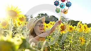 A little girl with Down syndrome walks in a sunflower field in the summer with a children's toy windmill.