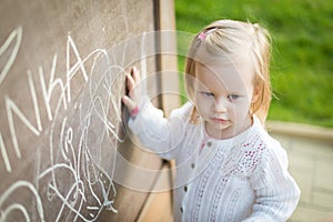 Little girl drawing on blackboard. Toddler girl having fun outdoors, holding chalk and drawing.