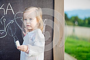 Little girl drawing on blackboard. Toddler girl having fun outdoors, holding chalk and drawing.