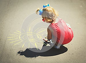 Little girl drawing sun on asphalt