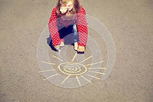 Little girl drawing sun on asphalt outdoors