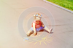 Little girl drawing sun with chalks on a street