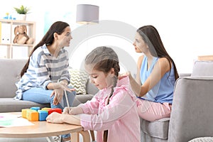 Little girl drawing at table while child psychologist talking