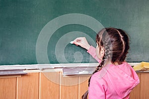 Little girl draws with chalk on a blackboard. The child performs a learning task. Babe starts school in first grade. School