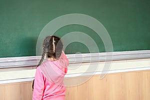 Little girl draws with chalk on a blackboard. View from the back. The child performs a learning task. Babe starts school in first