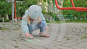 Little girl draws with chalk on a concrete tile sidewalk