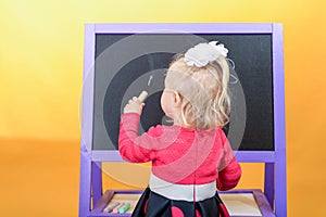 Little girl draws with colored chalk on a children`s school board. The concept of preschool education for children