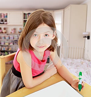 Little girl draws felt-tip pen on a white surface.