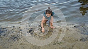 A little girl draws a heart on the wet sand at the water`s edge at sunset, sitting on her knees. The view from the top