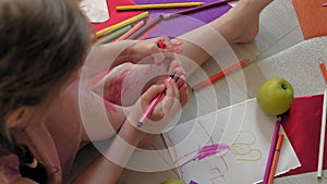 Little girl draws on her feet with felt-tip pens, children`s creativity, development