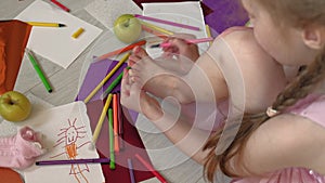 Little girl draws on her feet with felt-tip pens, children`s creativity, development