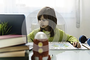 Little girl draws planet earth with wax colors on school notebook for Earth day while looking laptop for learning - Little