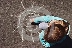 little girl draws the sun with chalk on the asphalt sidewalk