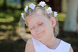 Little girl dreaming with eyes closed, child with a wreath of artificial flowers on her head