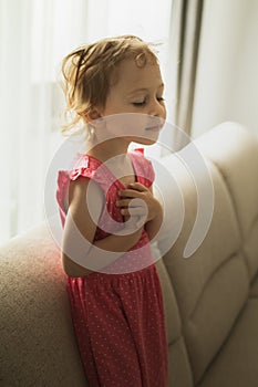 Little girl dreaming while sitting on a sofa next to a window