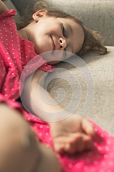 Little girl dreaming while sitting on a sofa next to a window
