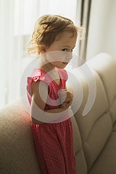 Little girl dreaming while sitting on a sofa next to a window