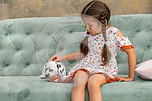 A little girl in a dress is gently stroking a Dalmatian puppy
