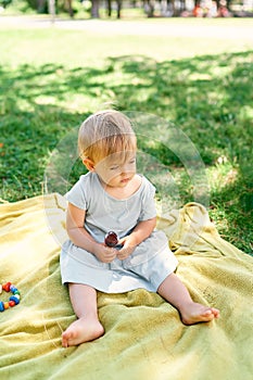 Little girl in a dress with ice cream in her hand sits on a bedspread on a green lawn