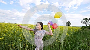 Little girl in a dress running through yellow wheat field with balloons in hand. slow motions