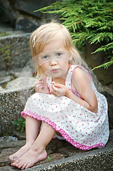 A little girl in a dress sits on the stone steps in the garden. Bare feet, smile