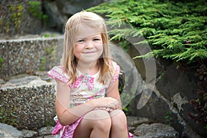 A little girl in a dress sits on the stone steps in the garden. Bare feet, smile