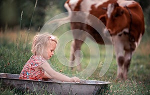 A little girl in a dress splashes in a trough of water in the middle of a green meadow.