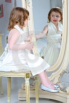Little girl dressed admires her reflection in mirror
