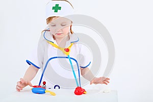 Little girl dressed as nurse plays with toy medical instruments