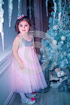 Little girl dressed in beautiful fashion white flower dress posing near Christmas tree