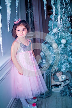 Little girl dressed in beautiful fashion white flower dress posing near Christmas tree