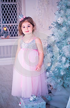 Little girl dressed in beautiful fashion white flower dress posing near Christmas tree