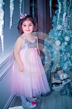 Little girl dressed in beautiful fashion white flower dress posing near Christmas tree