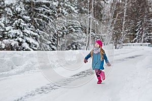 Little girl dressed in a blue coat and a pink hat and boots, fun runs through the winter forest