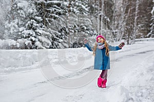 Little girl dressed in a blue coat and a pink hat and boots, hamming and playing in the winter forest