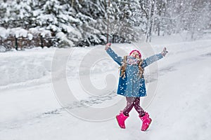 Little girl dressed in a blue coat and a pink hat and boots, hamming and playing in the winter forest