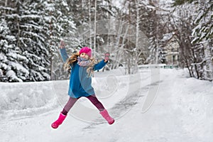 Little girl dressed in a blue coat and a pink hat and boots, high jumps winter forest