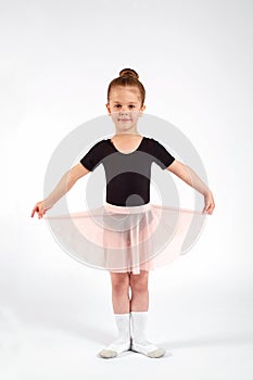 Little girl dressed in dance uniform is dancing over a white background in the studio.