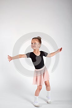 Little girl dressed in dance uniform is dancing over a white background in the studio.