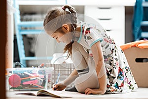 Little girl dressed in the dress and tights draws in the album sitting on the floor in the room photo