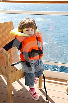 Little girl dressed in life jacket stands in cabin's balcony