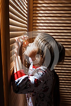 Little girl dressed in the pajama is hiding in the closet with wooden doors