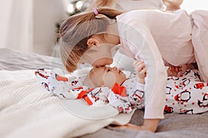 Little girl dressed in pajama kisses her tiny brother lying on the bed