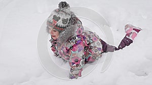 Little girl dressed in pink is the shoe, a bright jacket and cap with a pompon fooling around in the snow. She loves