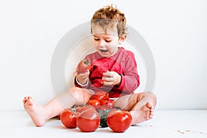 Little girl dressed in red squeezes tomatoes and makes a mess by savoring them