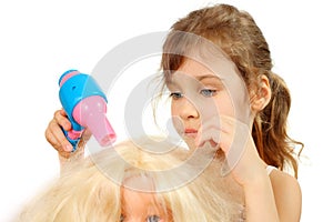 Little girl dries doll hair by toy hair dryer