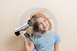 little girl dries her hair with a hair dryer with a comb attachment.