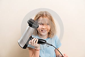 little girl dries her hair with a hair dryer with a comb attachment.